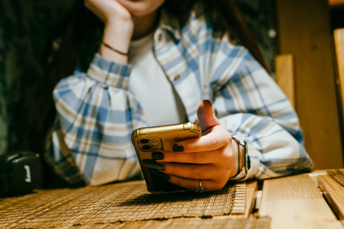 A teen holds a phone in her hand sitting at a kitchen table.