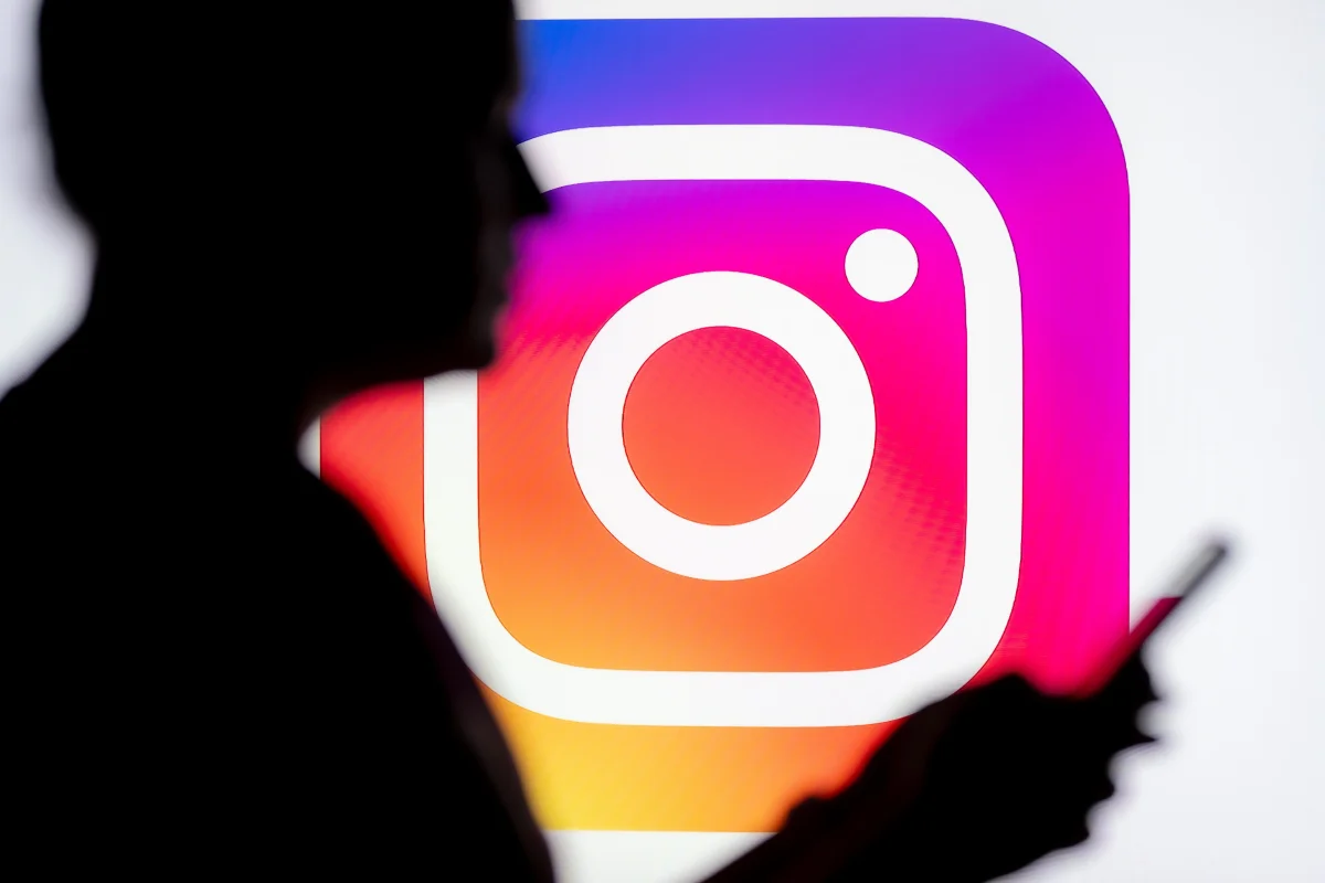 A person looks at a phone with the Instagram logo in the background.